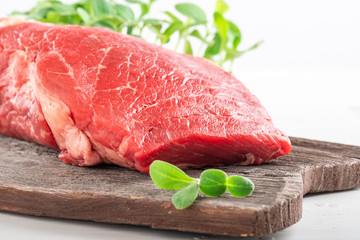 Fototapeta premium Fresh juicy piece of fresh beef with greens on a wooden Board on a white wooden background.