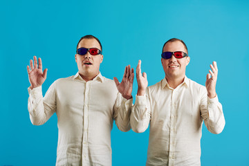 Caucasian twin brothers wearing white shirts and anaglyph 3D glasses looking at camera, bright blue...