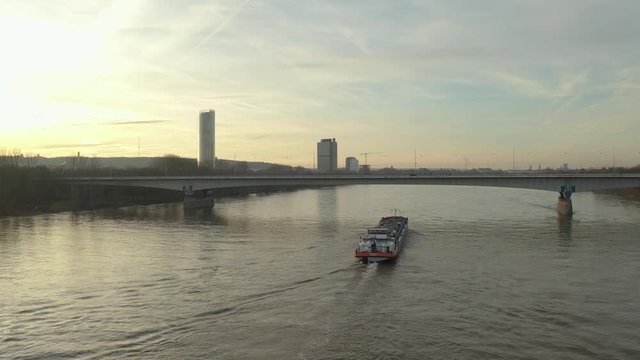 Cinematic drone / aerial shot of a ship on the river rhine in bonn with the post tower and the konrad-adenauer bridge at the golden hour, 30p