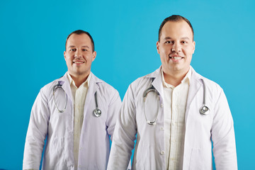 Horizontal studio portrait of twin brothers wearing white coats working as doctors standing against...