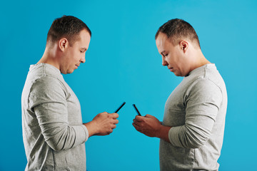 Twin brothers standing in front of each other using thier mobile phones, horizontal medium side view shot