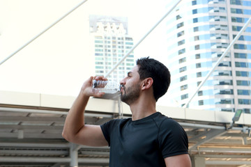 Young runner man drinking water after exercise run outdoor, hansom male jogger athlete training and doing workout in downtown city