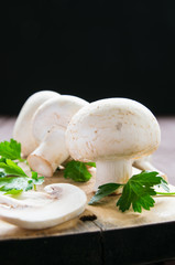 still life, champignon mushrooms with herbs on a cutting board on a wooden table