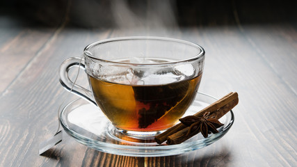transparent cup on a saucer with a tea bag, cinnamon sticks and anise on the table