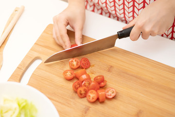 Cooking Salad. Female hands cut cherry tomatoes for Caesar.