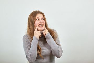 A young beautiful red haired woman in gray sweater insincerely forced fake laugh holding her index...