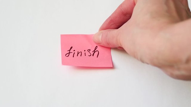 Hand sticks a sticker on a white background with the handwritten text "Finish".