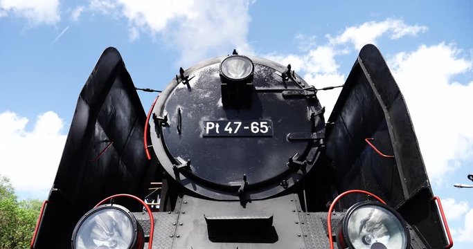 Low point of view time lapse over forefront antique steam train locomotive with license plate