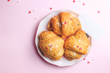 Valentine's day concept with two cups of coffee, almond croissant on pink plate on pink background. Top view,copy space. Romantic holiday. With empty card for your text