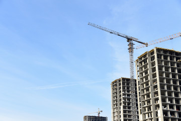 Tower cranes constructing a new residential building at a construction site against blue sky. Renovation program, development, concept of the buildings industry.
