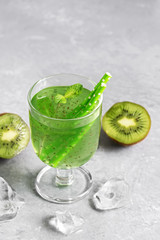 Kiwi cold refreshing drink in a glass with a straw and mint on a gray concrete background. Selective focus.
