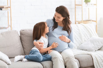 Pregnant woman and little daughter having conversation at home