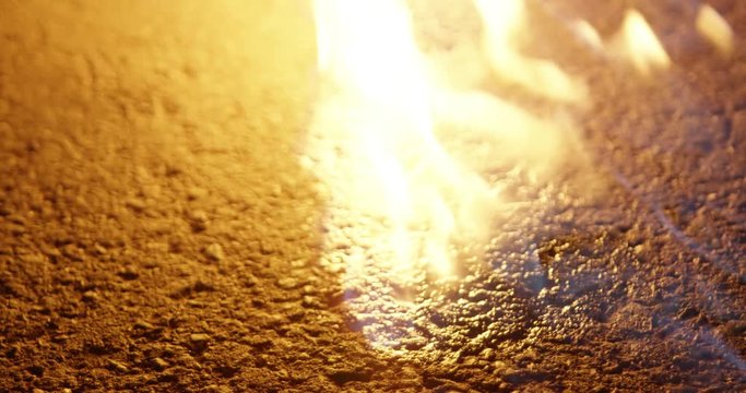 Close up shot of a hand with a lighter set fire / flame on the ground / on a road / street at night, 25p