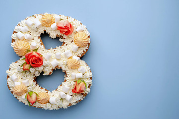 number 8 cake decorated with flowers, cream of cheese, marshmallows, Bizet on a blue background. International Women's Day postcard March 8