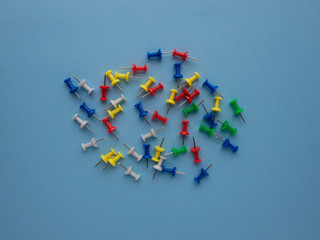 Different colors push pins isolated on blue background top view with copy space.