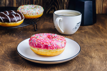 Colorful Donuts breakfast composition with different color styles of doughnuts and fresh coffee on wooden background. Selective focus