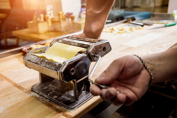 Chef rolling dough with a pasta machine. Pasta maker machine. 