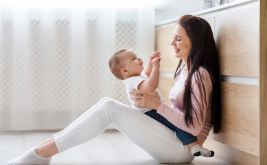 Cheerful mom tickling her toddler, playing on kitchen floor