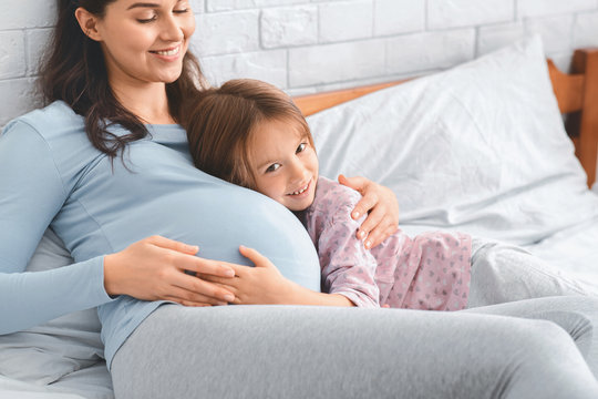 Little daughter and pergnant mother bonding on bed