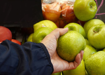 Supermarket image of woman hand taking  green apple  and holding the basket for shopping of fruit and vegetables in Supermarket store
