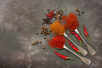 Assorted variety of spices pepper, paprika, chili, smoked paprika, hot pepper, peppercorns on a dark painted background. Top view, flat lay, copy space.
