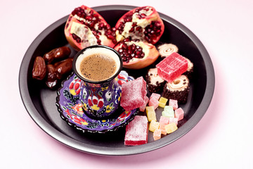 Fototapeta na wymiar Turkish Delight Turkish Coffee Date Fruit and Garnet on Black Round Tray Pink Background Close Up Ramadan