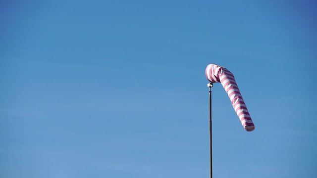 Windsock with red and white stripes show direction of wind blowing and speed. Cone wind indicator develops on blue sky background. Weathersock is in form of truncated cone made of fabric