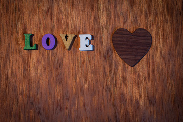 Inscription love and wooden heart on the background.
