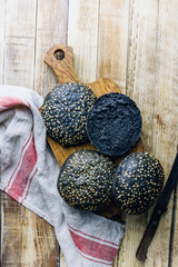 Sandwich or burger black buns colored with squid ink with sesame seeds on wooden background