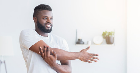 Cheerful african guy warming up, stretching hands at home