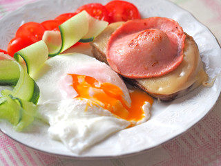 Ready-made Breakfast of eggs with liquid yolk, sausage and cheese sandwich decorated with tomatoes and cucumber slices