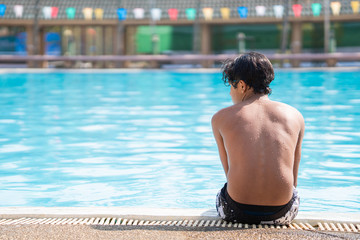 young boy sitting at the side of the swimming pool looking sad