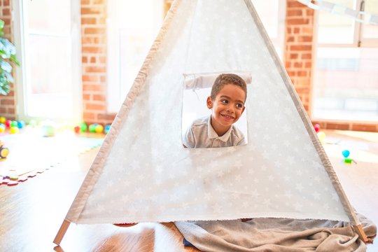 Beautiful african american toddler playing inside tipi smiling at kindergarten
