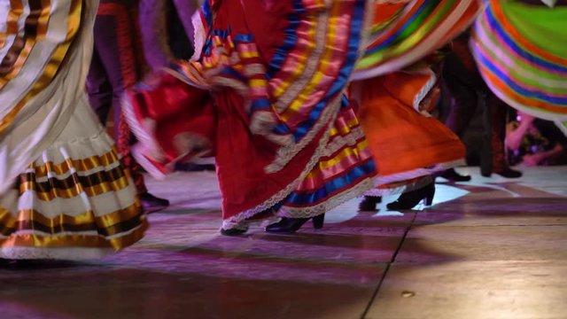 Closeup panning shot of women doing Mexican folk dance with their dresses curling through the air.