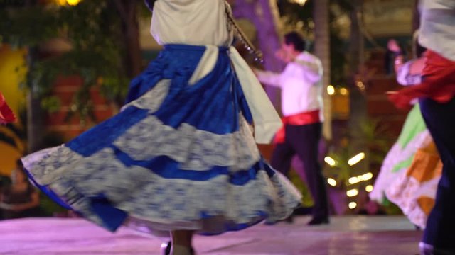 Mexican folk dancers spin in circles with their arms raised.