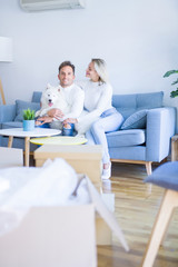 Obraz premium Young beautiful couple with dog sitting on the sofa at new home around cardboard boxes