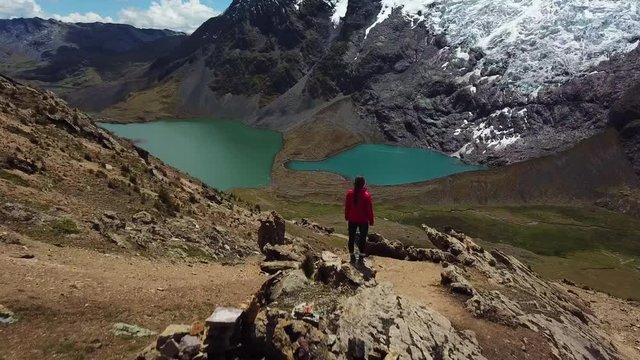Aerial, drone shot over a woman on a cliff, in front of a glacier and Ausangate Mountain, on a sunny day, in the Andes mountains, near Cusco, Peru, South America