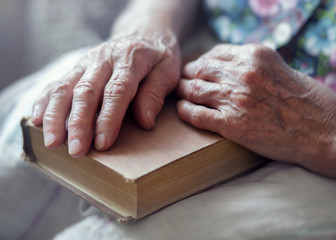 Hands of an old woman lying on a book. An elderly woman holds an old book in her hands.