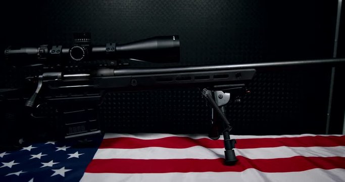 black Sniper Rifle with high powered Scope and ten round Magazine on American flag with dark background, right hand side view, slow pan right to left, 4k