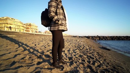 Elderly woman standing on beach with bag hat and sunglasses. Pedestal up