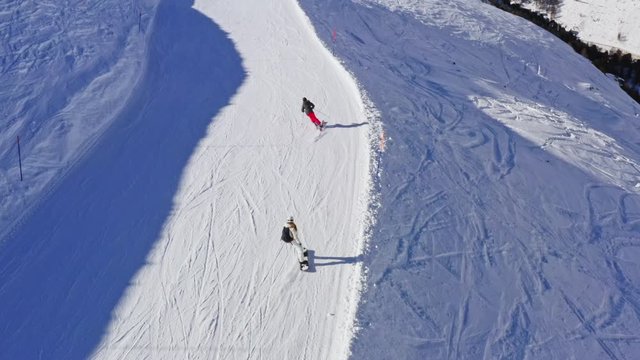 Aerial Following Shot fo Skier And Snowboarder Going Down the Snowy Slope.
Drone View of Professional Skiers Speeding Downhill.