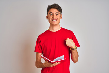 Teenager student boy reading a book over isolated background with surprise face pointing finger to...