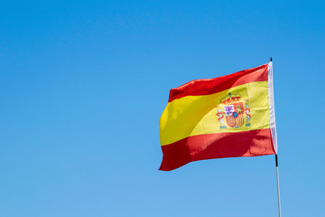 a Spanish flag blowing in the wind with blue skies in the background in Marbella, Spain