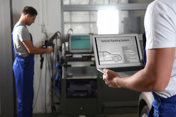 Mechanic with laptop doing car diagnostic at automobile repair shop, closeup. Space for text