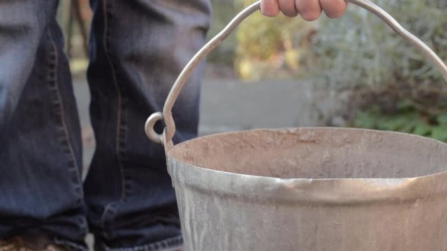 Lady picking up metal bucket on garden pathway close up