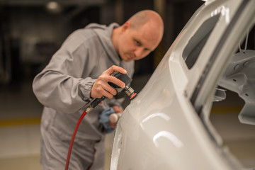 A worker in the paint shop of an automobile plant grinds painted body elements