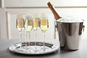 Glasses of champagne and ice bucket with bottle on grey table