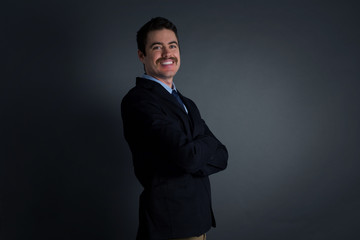 Portrait of thoughtful smiling man keeps hand under chin, looks directly at camera, listens something with interest, dressed casually, poses against gray wall. Youth concept.