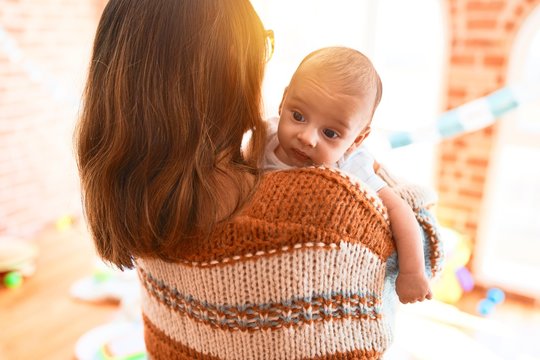 Young beautiful woman and her baby standing at home. Mother holding and hugging newborn