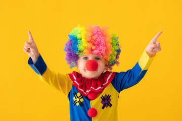 Funny kid clown playing against yellow background